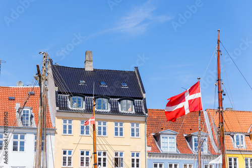 Danish flag waves background Nyhavn colorful house buildings in canal harbor Copenhagen sightseeing tourist travel destination in Denmark on sunny day. Clear blue sky backdrop © Kirill Gorlov