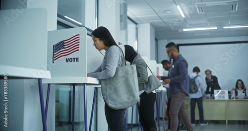 Asian woman comes to voting booths in polling station office. National Election Day in United States. Political races of US presidential candidates. Concept of civic duty and patriotism. Dolly shot. photo