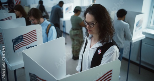 National Election Day in United States. Woman in glasses votes in booth in polling station office. Political races of US presidential candidates. Civic duty and patriotism. Slow motion. Dolly shot. photo