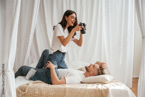 Woman is taking photo of man by camera. Young couple are together at home