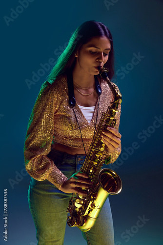 Photography Portrait of young attractive woman, saxophonist performing jazz melodies in neon light against gradient background