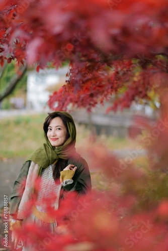 Asian woman in a fashionable sweater revels in the beauty of fall. A pretty and cheerful portrait amid nature's vibrant colors.