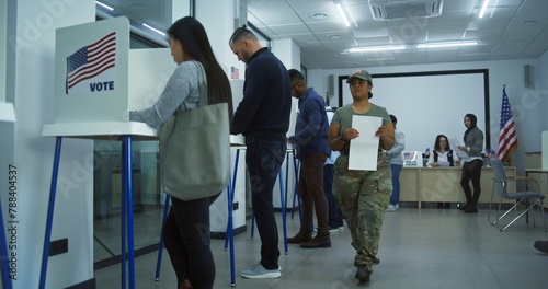 Diverse American citizens vote in booths in polling station office. National Election Day in United States. Political races of US presidential candidates. Civic duty concept. Slow motion. Dolly shot. photo