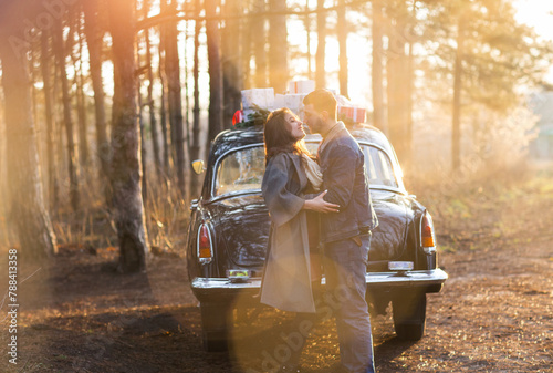 Happy couple hugging and flirting standing near vintage car in woods