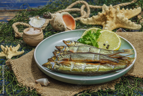 Smoked smelt with fresh lemon and herbs. Salted fish with marine decor. Trendy dish, sea rope photo