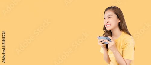 Cheerful young woman in yellow top smiling while holding and looking at smartphone against a yellow background.
