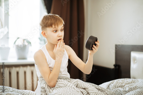 Kid boy teenager waking up shocked looking alarm clock in morning