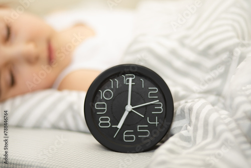 Alarm clock on bed. Cute kid girl sleeping on the background.