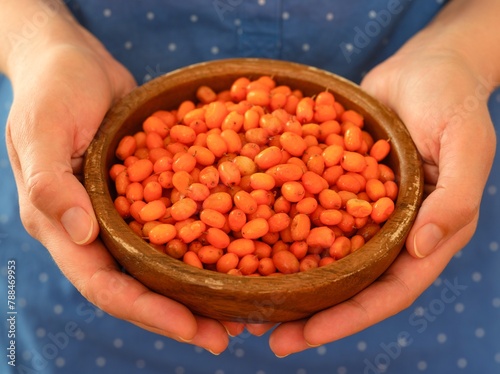 Woman holding wooden bowl full of frozen ripe sea buckthorn berries in her hands. Close-up