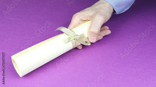 Man's hand holds a scroll of graduation or award, with purple background.
