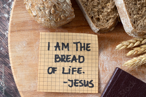 I am the bread of life, Jesus Christ, handwritten text note with wheat and closed holy bible book on wood. Top view. Christian biblical concept of spiritual food, salvation, and faith in God.