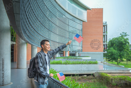 Young Asian student stands holding an American flag on campus. Looking and smiling happily