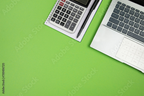 office desk with laptop calculator and other office supplies on isolated green background with copy space.