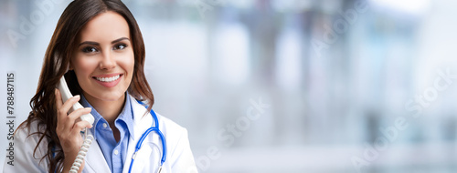 Portrait of happy smiling female doctor on phone, against blurred modern office background. Medical call center concept picture. Wide banner composition image with empty ad slogan text area.