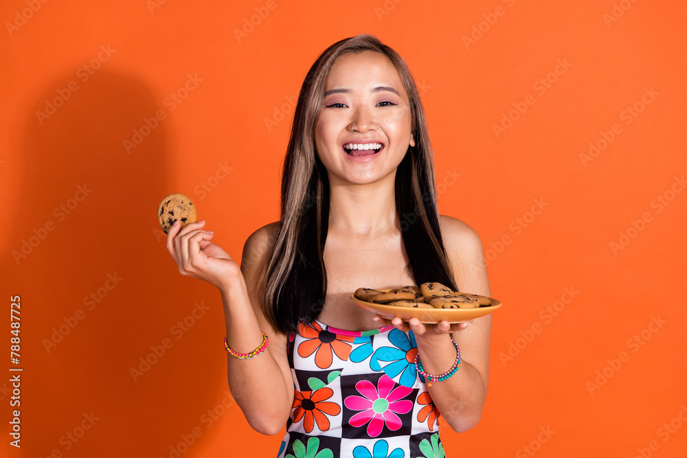 Portrait of overjoyed lovely woman with dyed hairstyle dressed print tank holding tasty cookies isolated on orange color background Portrait of overjoyed lovely woman with dyed hairstyle dressed print tank holding tasty cookies isolated on orange color background