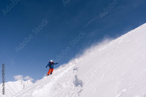 Woman snowboarder riding on slope of powdery snow in high mountains. Freeride in avalanche-prone area, amazing mountain peaks view