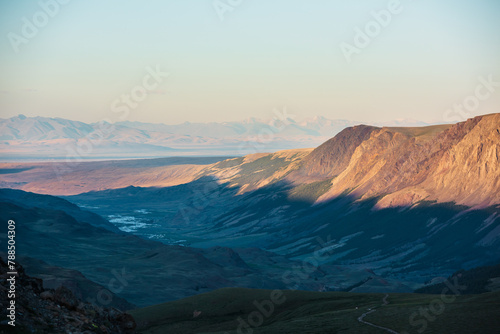 Scenic aerial top view to gold sheer crags on mountain ridge, illuminated by setting sun under clear sky in golden sunset tones. Evening alpine landscape in sunset color. Light and shadow in mountains