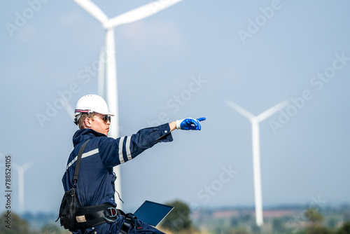 Focused engineer with a laptop conducts field analysis at a wind farm, wind turbines towering in the background.