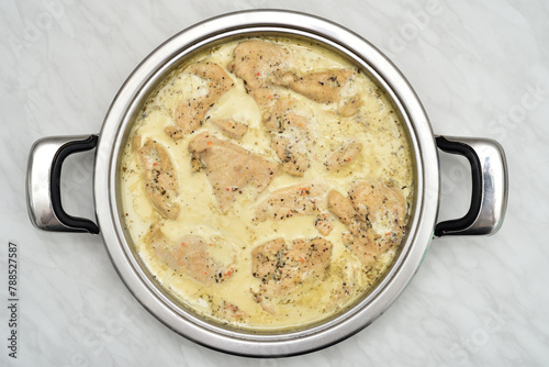 Grilled chicken breast fillets with cooking cream and herb spices in the steel frying pan on the light gray marble table texture. Top view. 

