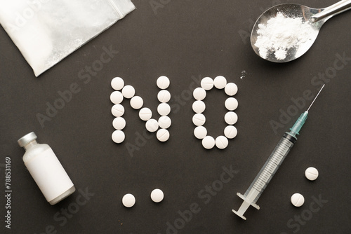 International Day against Drug Abuse. Top view of NO text made from pills with syringe and drug powder on black background. Stop drug addiction concept.