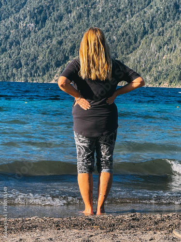 A woman stands on the beach, looking out at the ocean. She is wearing a black shirt and black pants