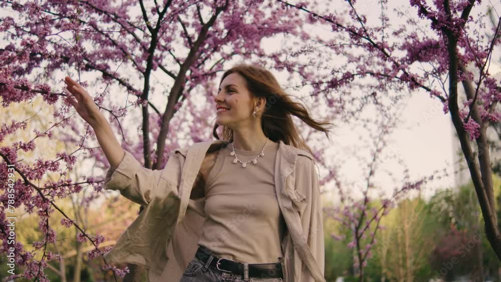 beautiful girl walks in the park among pink spring trees. Young Woman enjoying the spring mood beautiful girl walks in the park among pink spring trees. Young Woman enjoying the spring mood