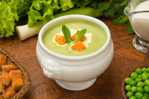 French pea soup "Saint Germain" in a white tureen with ingredients on a brown table.