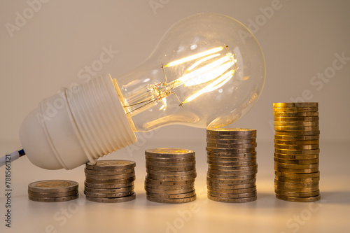 Light bulb lit, above stacks of coins. Increase in electricity tariffs, energy dependence, energy supplies.
