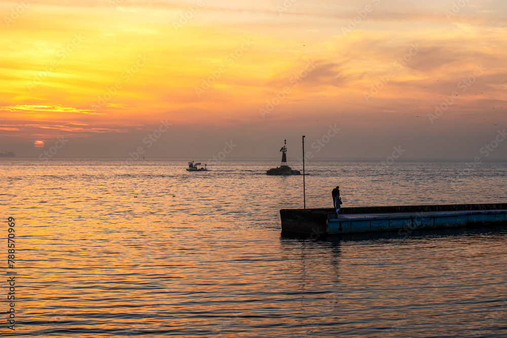 Sunset on the sea with boats and people on the pier