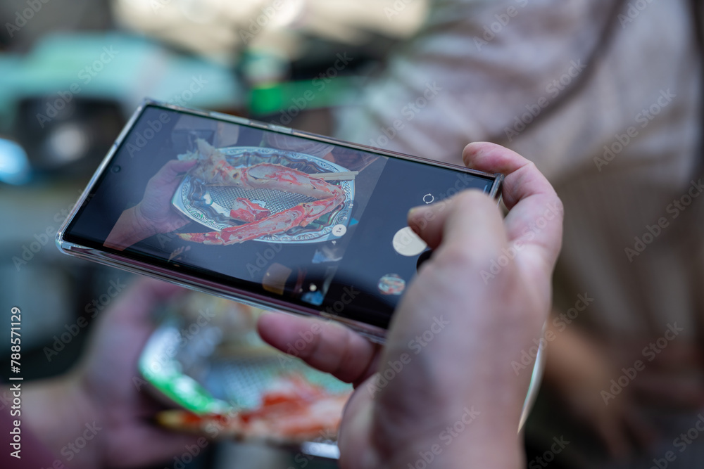 Close-up of a person's hands using a smartphone to photograph a colorful dish, emphasizing the intersection of technology and culinary arts.