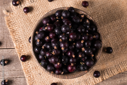 Black currant in a bowl on wooden background. Organic berries. 