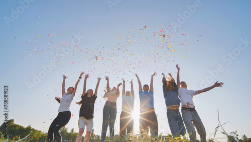 Friends toss colorful paper confetti from their hands against the rays of the evening sun.