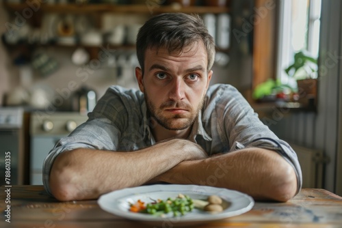 Loss of Appetite - Portrait of Depressed Caucasian Man with Aversion to Diet in Front of Dinner Plate, Concept of Anxiety and Appetite Suppressant photo