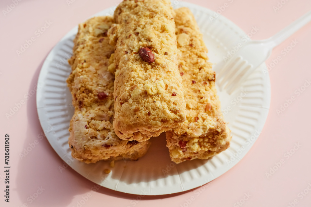 Creamy cake with nuts on a paper plate with a plastic fork on a pink background, nut dessert on disposable dishes, a portion of cake with nuts