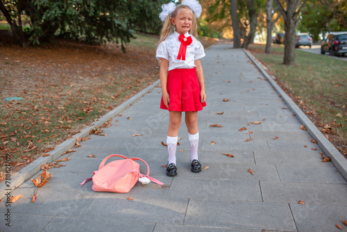 A Girl in uniform with backpack crying on the street