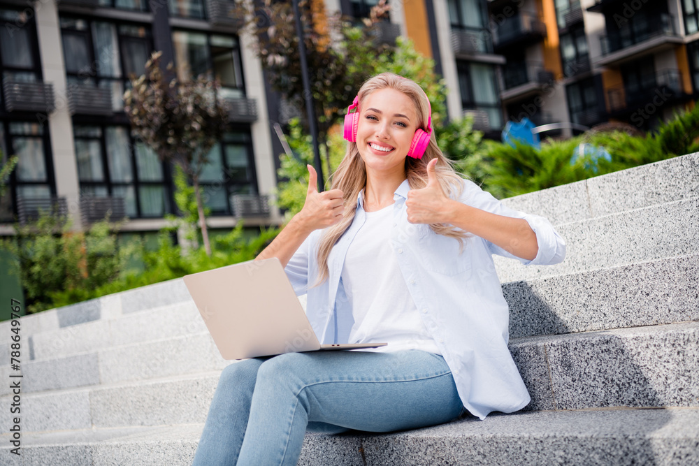 Fototapeta premium Portrait of adorable satisfied cute girl sitting on stairs fresh air working remotely showing thumbs up summer outdoors