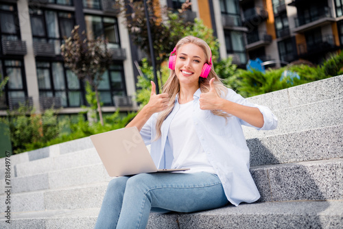 Portrait of adorable satisfied cute girl sitting on stairs fresh air working remotely showing thumbs up summer outdoors