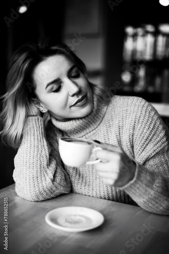 Cozy Coffee Break. A woman in a sweater enjoys a moment of relaxation, her head resting on her hand as she savors a cup of coffee at a table, exuding comfort and tranquility.