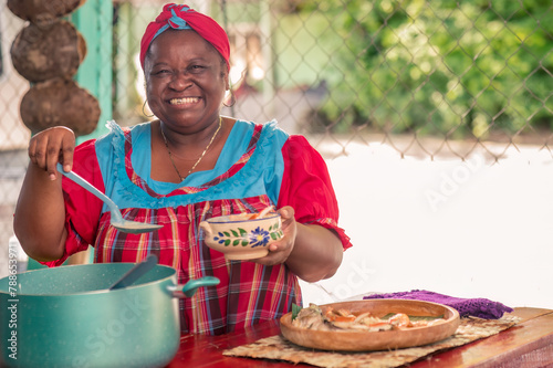 A beautiful African American woman on the patio of her house serving soup. A senior adult woman smiling and looking at the camera as she serves a plate of food. 