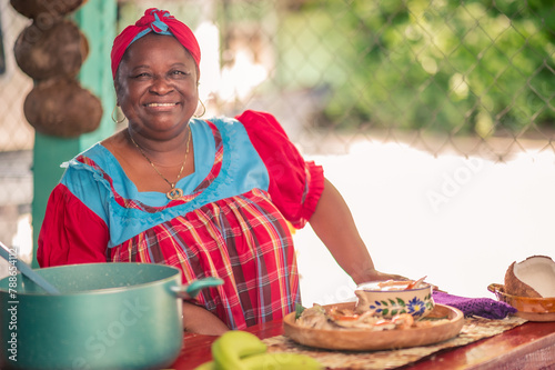 Portrait of an adult woman standing in her kitchen looking at a camera. Proud African American woman in colorful Garifuna dress.