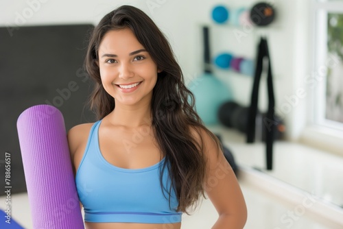 Smiling young attractive hispanic woman posing wearing a sport outfit holding a yoga mat looking at the camera