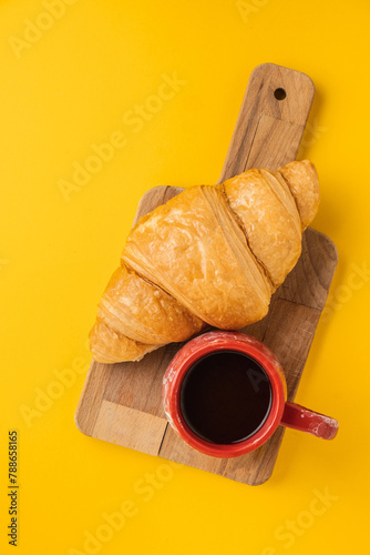 Flat lay of freshly baked croissants on the yellow background. Traditional French pastry with a cup of black coffee. Copy space for a free text