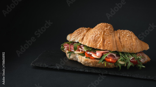 Freshly baked croissant with iberian ham, tomatoes and salad filling isolated on black background. Mock up of croissant with copy space for a free text