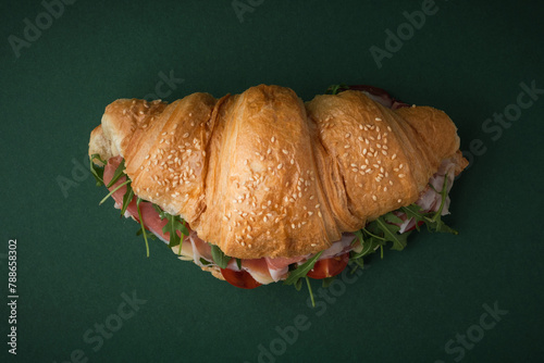 Freshly baked croissant with iberian ham, tomatoes and salad filling on dark green background. Mock up of croissant with copy space for a free text