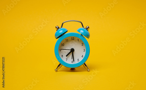 Round alarm clock on a yellow background, half past seven in the morning.