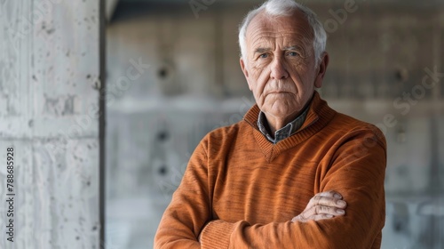 Elderly man with crossed arms wearing orange sweater. High-resolution studio portrait with a concrete background. photo