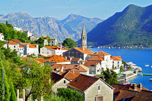 View of the Montenegrin city of Perast: the old houses of the city and the famous bell tower of the Church of St. Nicholas against the backdrop of the sea and mountains.