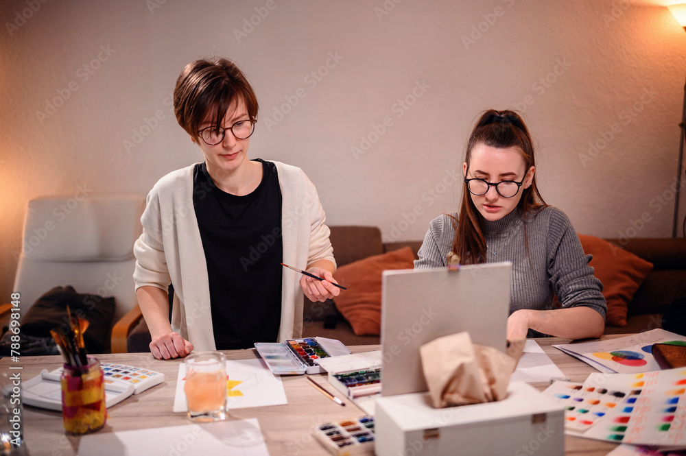 Two focused designers collaborate on an artistic project, one painting while the other evaluates the work, amidst a creative studio atmosphere