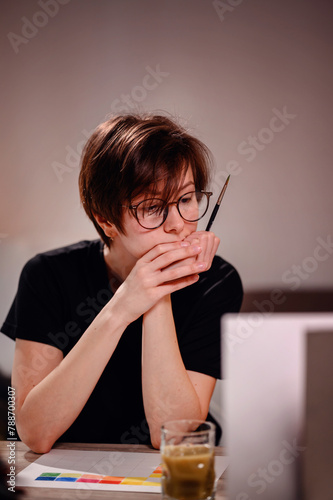 An artist pauses for reflection, brush in hand, as she contemplates her next stroke on a color chart, embodying the thoughtful nature of the creative process photo