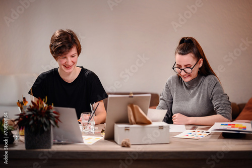 A candid shot of two artists at work, one smiling at her creation while the other is engrossed in detail, capturing the joy and focus of artistic collaboration. photo